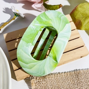 Detail of large oval hair claw clip with green marble texture on wooden display tray