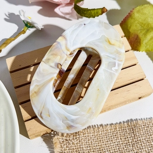 Detail view of oval acetate hair claw with marble texture on wooden display stand