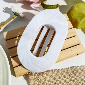 Detailed macro of white marble acetate hair claw clip on an aesthetic wooden tray