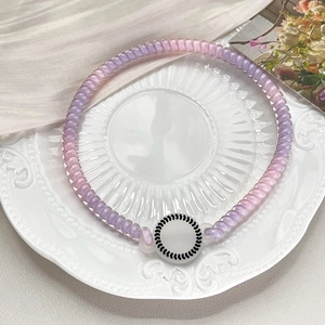 Close-up of a purple and pink gradient spiral hair tie with a white circular pendant