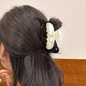 Pince à cheveux en acrylique nacré blanc avec lettre K dorée portée sur cheveux noirs