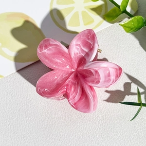 Détail de la texture marbrée rose et blanc sur une pince à cheveux fleur de frangipanier