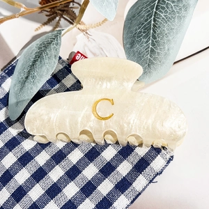 Détail de la pince à cheveux en acétate crème avec emblème lettre C dorée élégante