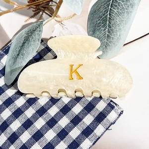 Détail de la pince à cheveux en acrylique crème avec lettre K dorée et fini pailleté