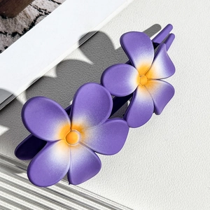 Macro shot of gradient purple frangipani hair clip on a white textured background