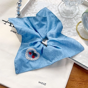 Détail d'un chouchou à carreaux bleu clair avec bordure en dentelle blanche et motif cerise