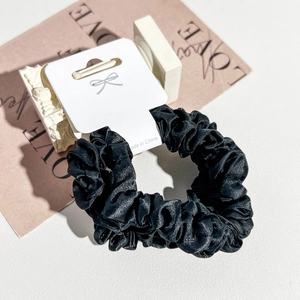 Detail of satin scrunchie with pleated texture on white presentation card packaging