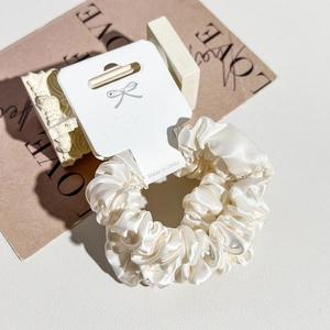 Cream satin hair scrunchie with high-gloss texture on white display card with decor