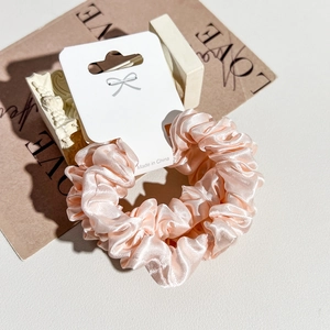 Detailed view of a premium pink satin scrunchie displayed on a minimalist gift tag
