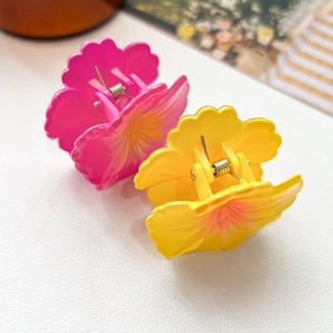 Detail view of pink and yellow floral hair claws with wavy petal texture on a white surface