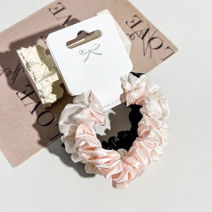 Detailed view of pink, white and black satin scrunchies set on elegant card display