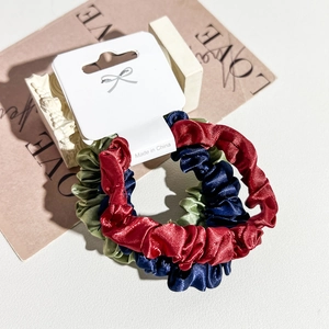 Three-pack of satin silk scrunchies in red, navy blue, and green on a display card