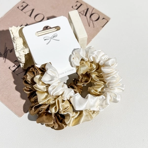 Detailed close-up of three satin silk scrunchies in gold tones on a premium card display