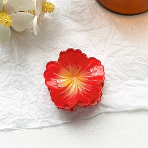 Macro detail of red translucent acrylic flower hair claw clip with gradient petal texture