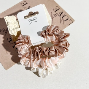 Close-up of three satin scrunchies in bronze, champagne, and white on a display card