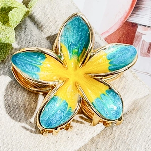 Macro detail of Frangipani hair claw with golden metal teeth and blue-yellow petals