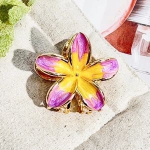 Macro shot of purple enamel frangipani flower hair claw clip with golden metal base