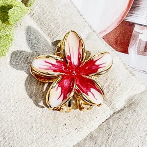 Close-up of golden metal frangipani hair claw with gradient rose red enamel finish