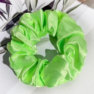Vue détaillée d'un chouchou en satin vert néon avec texture plissée sur motif de feuilles