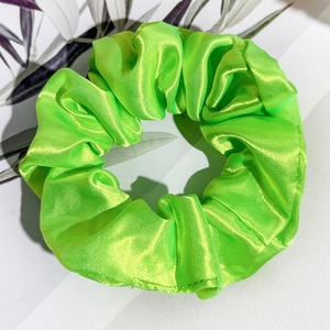 Détail d'un chouchou en satin vert néon avec texture plissée brillante sur fond blanc