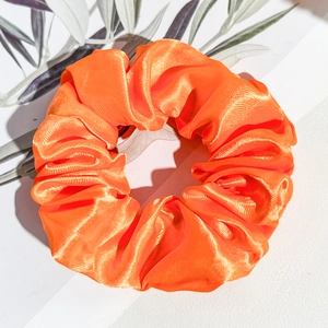 Gros plan sur un chouchou en satin orange vif avec texture soyeuse et plis élégants