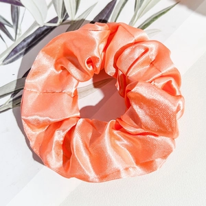 Détail d'un chouchou en satin corail montrant une texture soyeuse et un design plissé