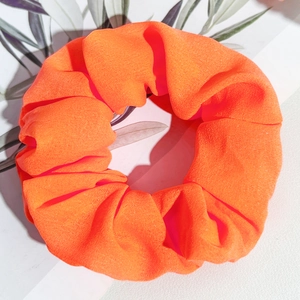 Vue détaillée du chouchou en tissu orange vif avec une texture plissée douce sur fond blanc