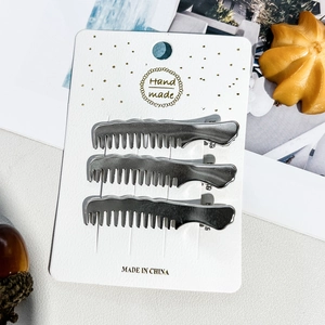 Lot de trois barrettes à cheveux en métal argenté en forme de peigne sur carte