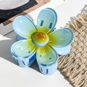 Gros plan d'une pince à cheveux fleur de frangipanier bleu et jaune sur cuir blanc