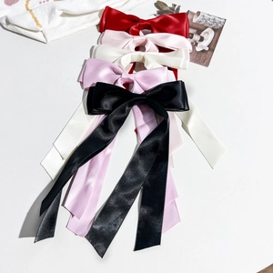 Détail de cinq barrettes à nœuds en satin coloré avec de longs rubans sur fond blanc