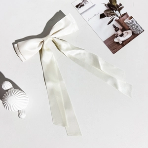 Gros plan d'une pince à cheveux en satin blanc crème avec de longs rubans élégants
