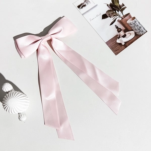 Détail de la barrette à cheveux nœud en satin rose avec rubans sur fond texturé blanc décoré