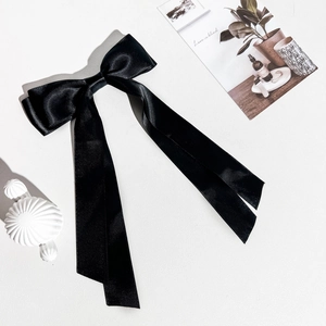 Détail d'une pince à cheveux en satin noir avec de longs rubans sur fond blanc texturé