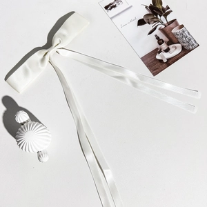 Détail d'un nœud en satin blanc crème avec de longs rubans sur une surface blanche texturée