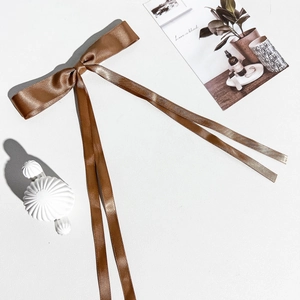 Détail d'un nœud papillon à longs rubans marron en satin brillant pour les cheveux