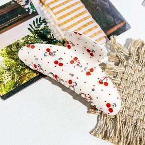 Detailed view of large white claw clip with red cherry prints and sparkling rhinestones