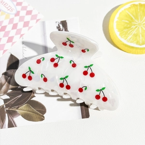 Détail d'une pince à cheveux en PVC blanc avec motif cerise rouge et ressort doré robuste