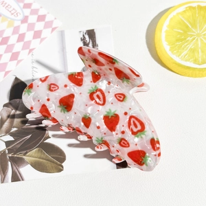 Détail d'une pince à cheveux blanche semi-transparente avec motif fraise rouge