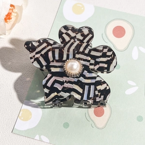 Detail of flower hair claw with marble texture, large center pearl, and gold metal base