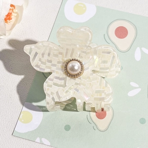 Detail shot of pearl flower claw clip with iridescent acetate texture on a green background
