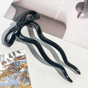 Detail of elegant black ribbon bow U-shaped hair pin with glossy finish on white leather