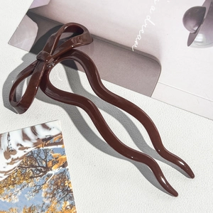 Detail view of a brown resin bow hair pin featuring a wavy double-prong design