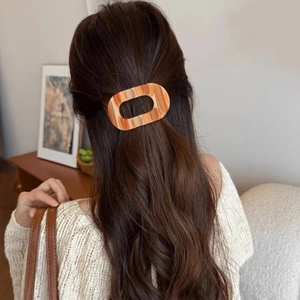 Flat oval hair claw clip with colorful marble pattern on dark brown wavy hair