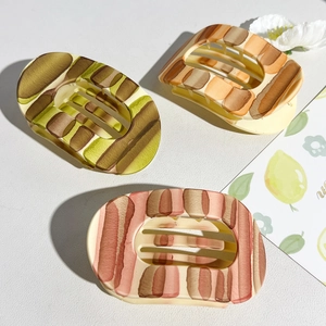 Close-up of matte resin hair claws in green, orange, and pink striped patterns