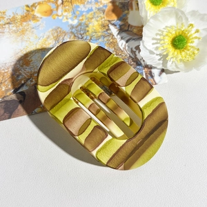 Detail of flat oval hair claw clip with colorful geometric patterns on white leather