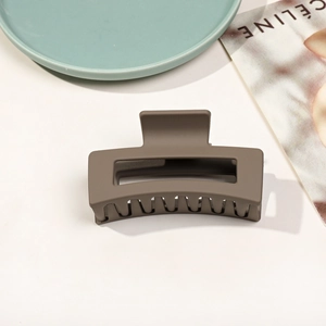 Détail d'une pince à cheveux rectangulaire mate taupe sur un fond esthétique minimaliste