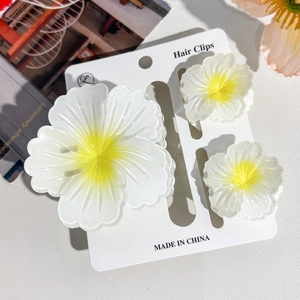 Detailed view of three white plumeria flower hair claws on a cardboard display card