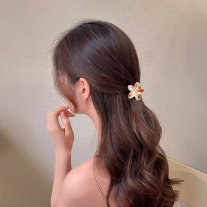 Floral plumeria hair claw with red and white patterns on a model's long wavy hair