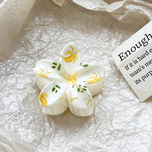Detailed macro shot of a white frangipani hair claw clip with vibrant yellow banana prints