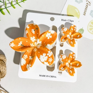 Detailed set of orange floral hair clips with white daisy print and matte plastic finish